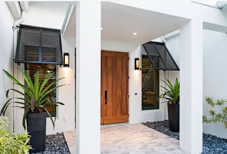 Dark Bahama shutters beside a wood front door on a white home