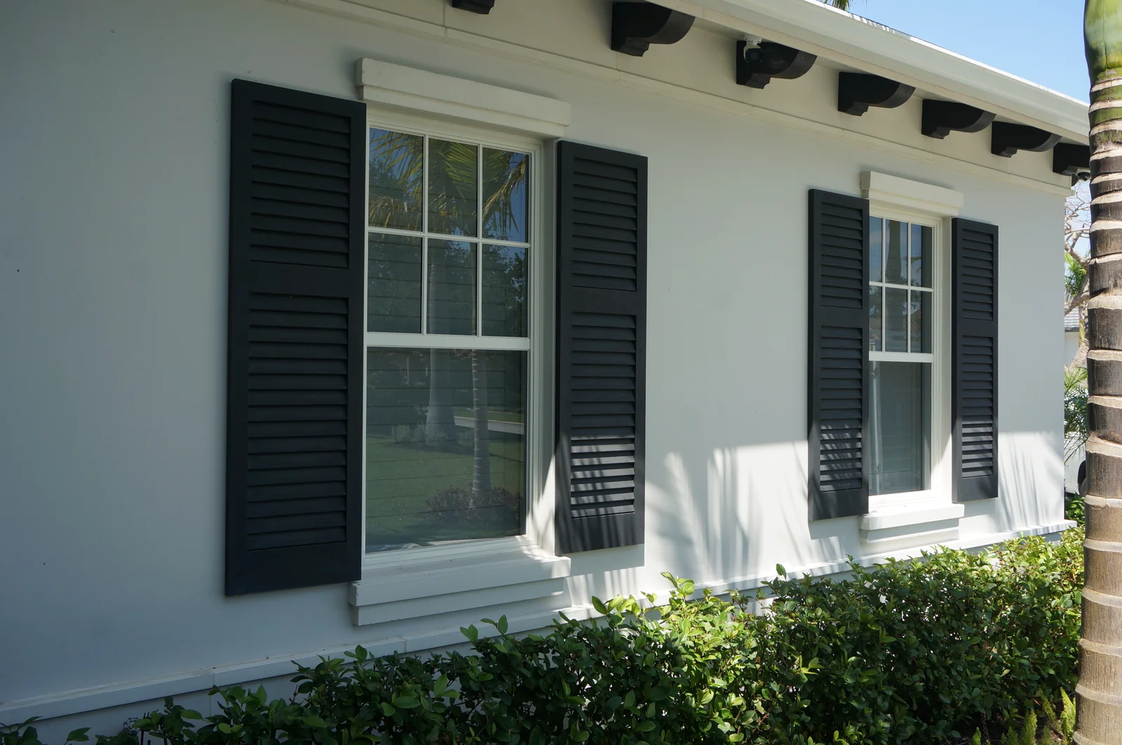 Dark louvered Colonial shutters framing two windows on a white exterior wall